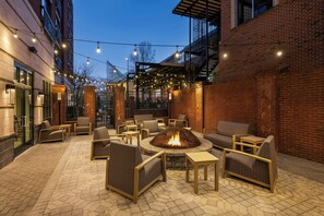 An outdoor patio with wicker furniture, a central fire pit, and string lights.