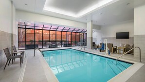 An indoor swimming pool with clear glass walls, a tiled floor, and a seating area with chairs and tables. - Courtyard by Marriott Chattanooga Downtown (Chattanooga)