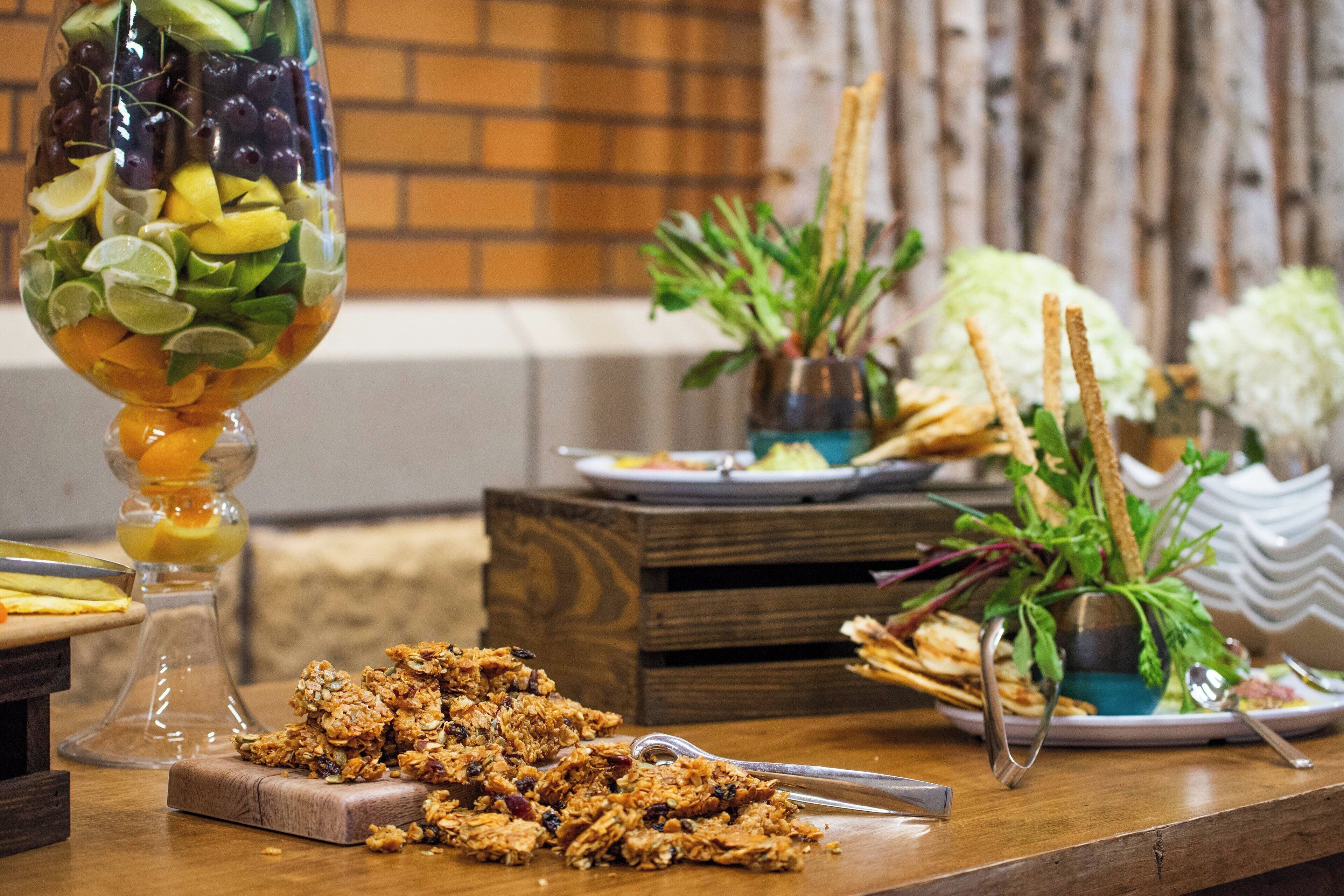 A wooden table with a glass fruit bowl, a plate of granola, and a small plant.