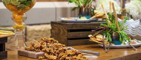 A wooden table with a glass fruit bowl, a plate of granola, and a small plant.