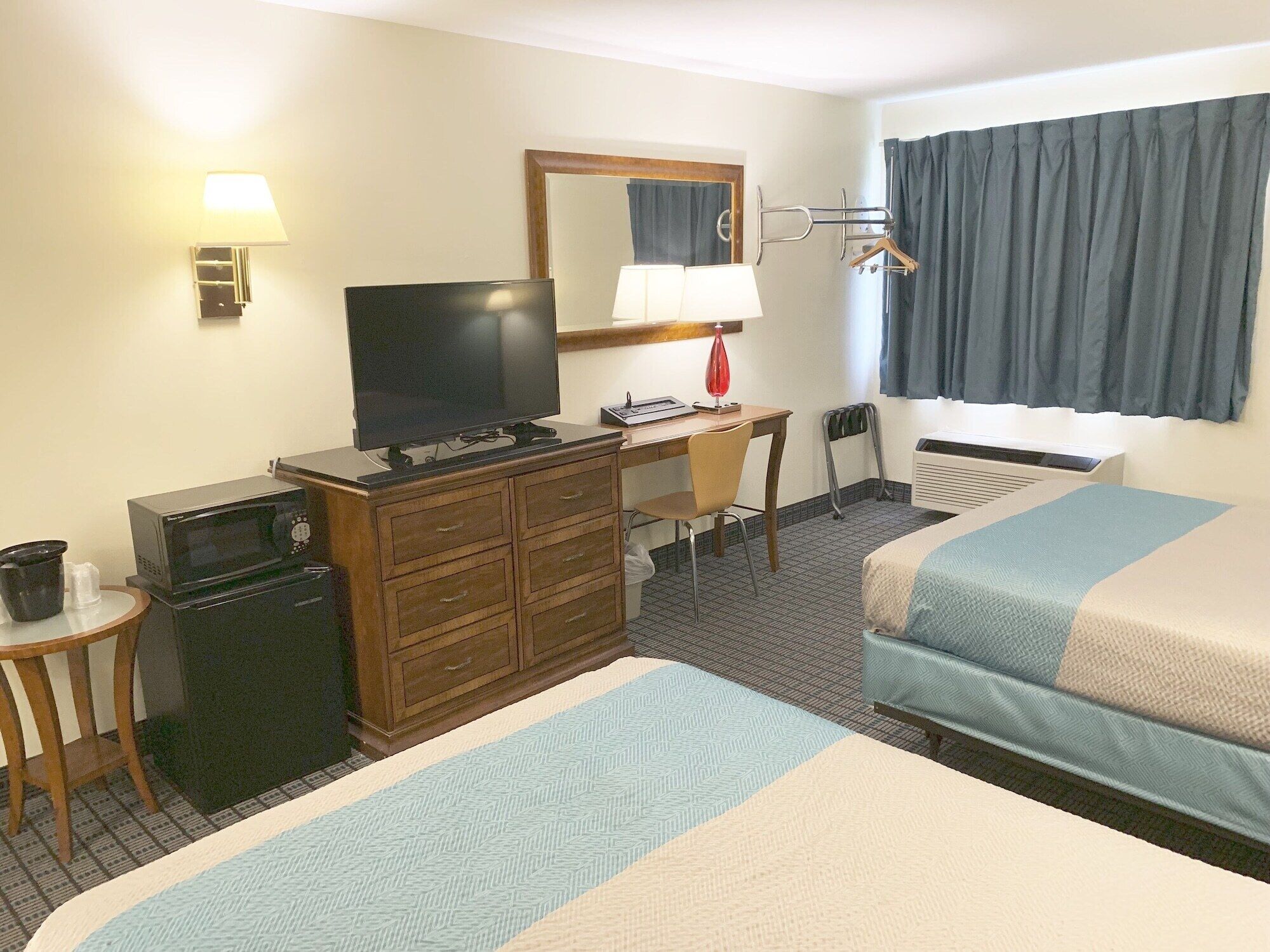 A hotel room with two beds, a desk with a computer, a television, and a microwave.