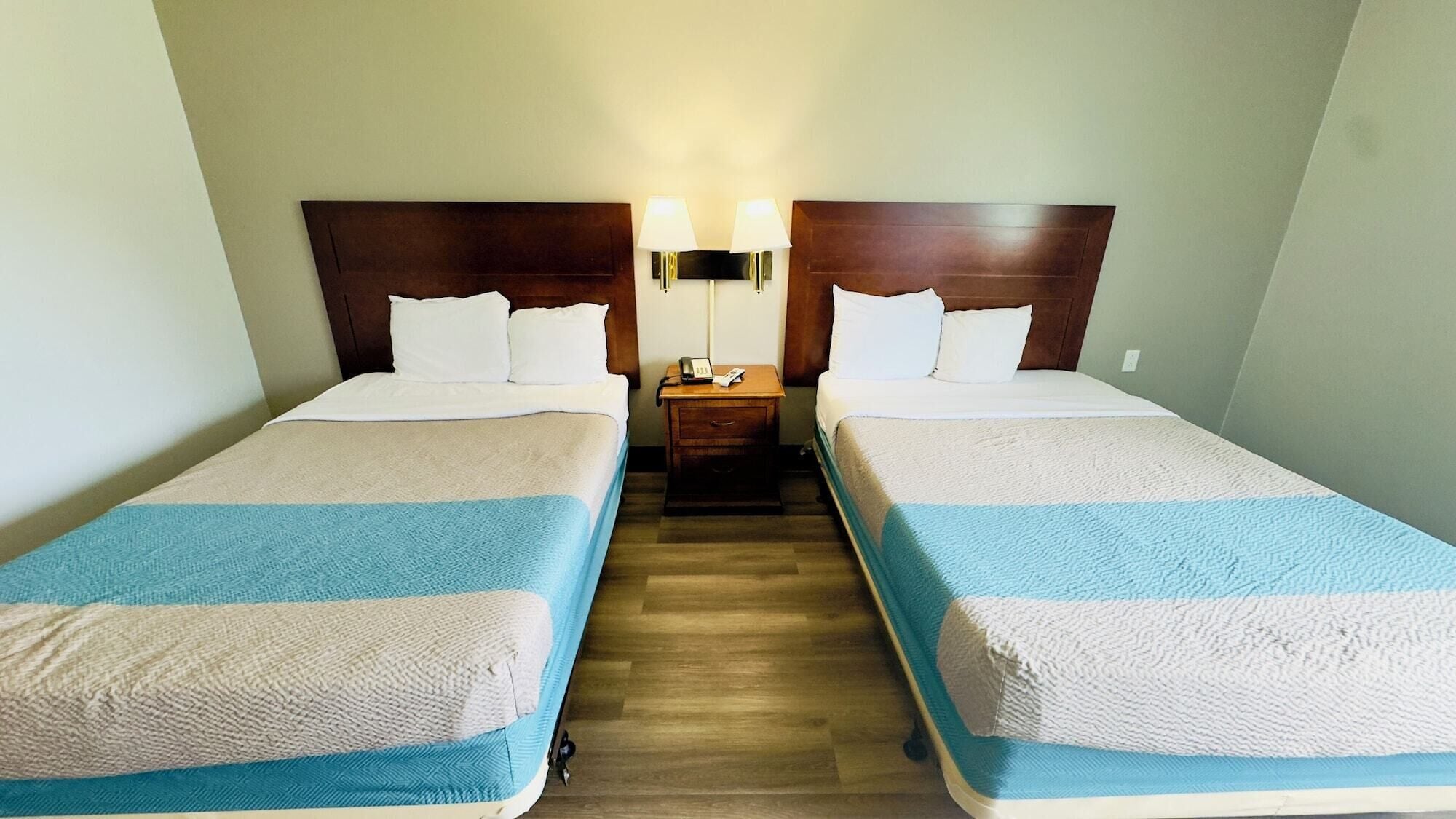 A hotel room with two single beds, a wooden headboard, a nightstand with a lamp, and a telephone.