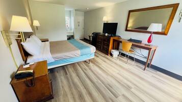 Habitación de hotel con cama, mesita de noche, lámpara, escritorio, silla, televisión y espejo.