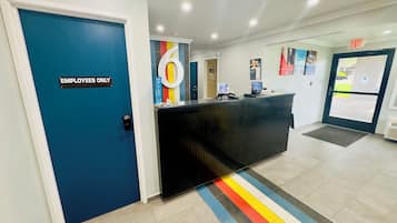 Un área de recepción con una puerta azul que indica 'SOLO PERSONAL', un mostrador de recepción negro y una alfombra colorida a rayas.