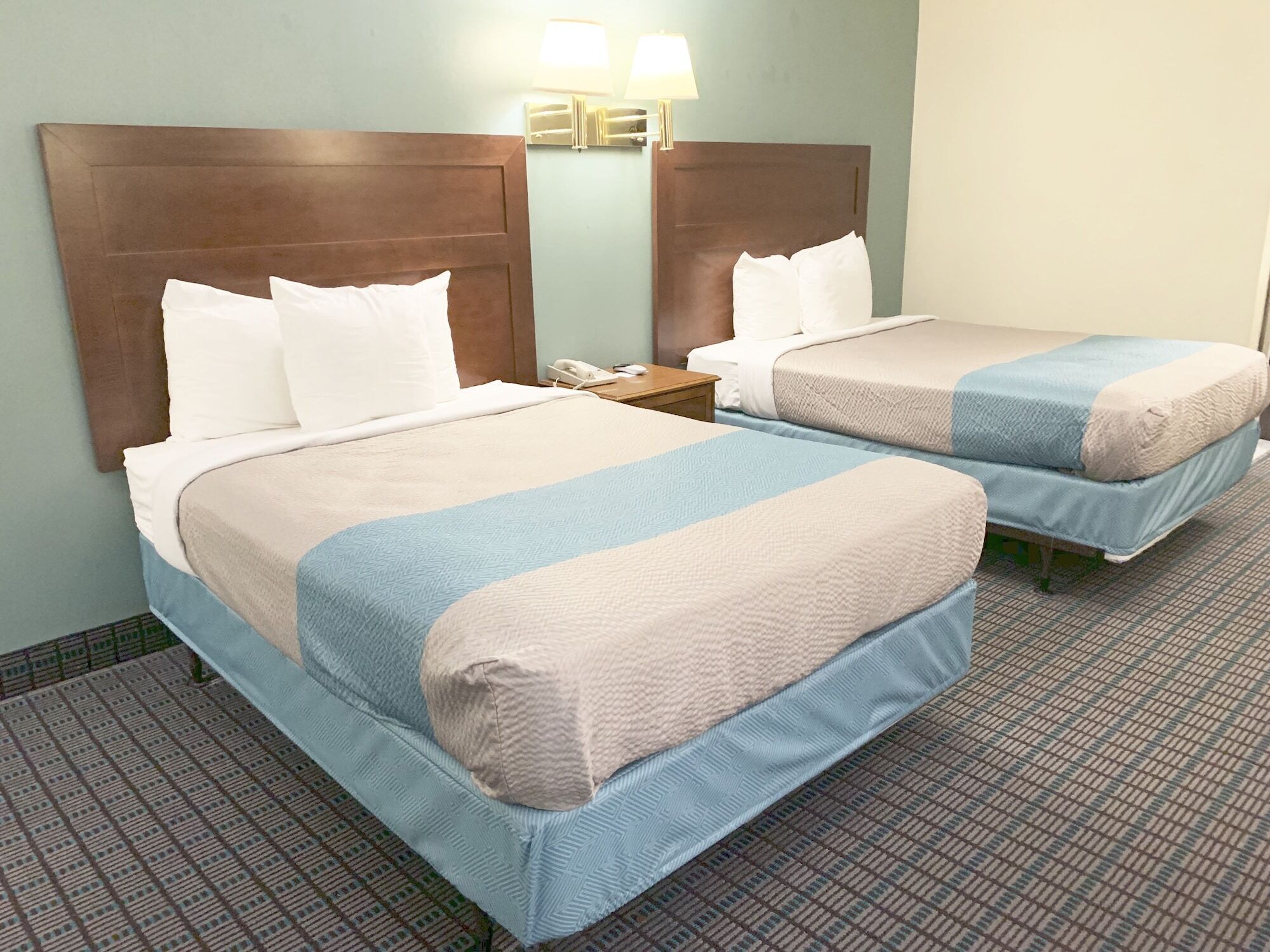 Ein Hotelzimmer mit zwei Betten, jeweils mit Kopfstütze, Nachttisch und Lampe.