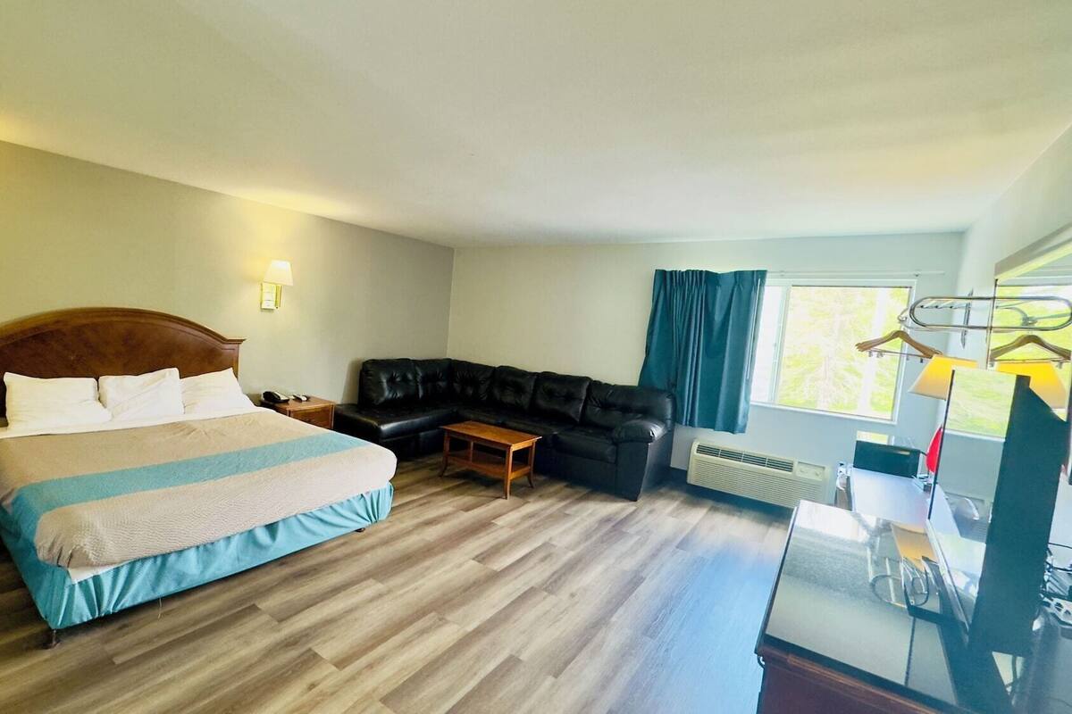 A hotel room with a bed, a black leather sofa, a small table, and a window with curtains.