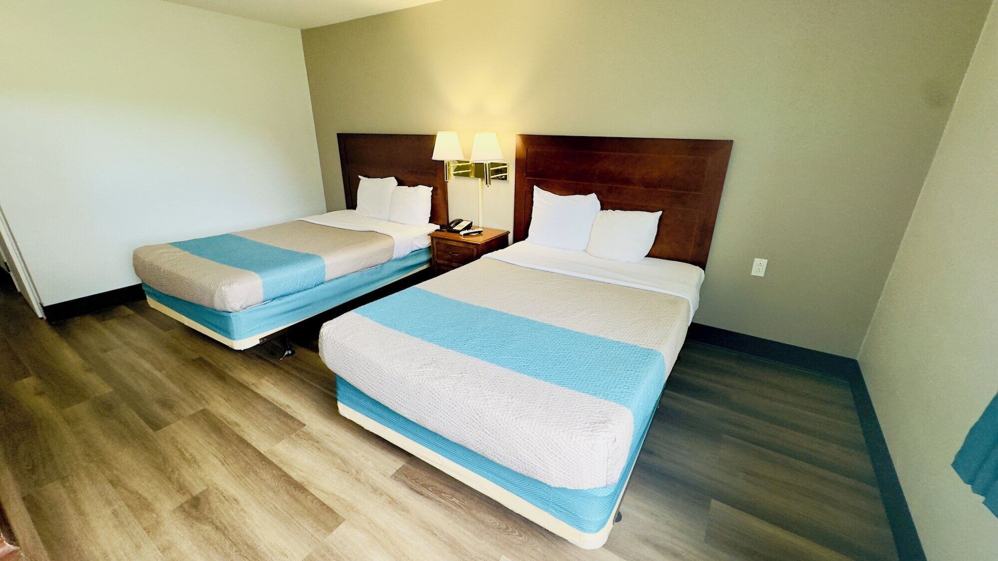 Habitaci ón de hotel con dos camas, cada una con cubrecama a rayas, cabecero de madera, mesita de noche con lámpara y teléfono.