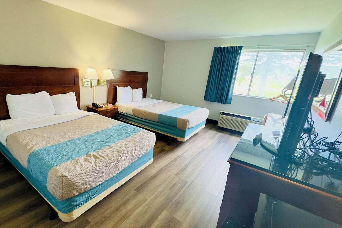 A hotel room with two beds, a desk, and a television.