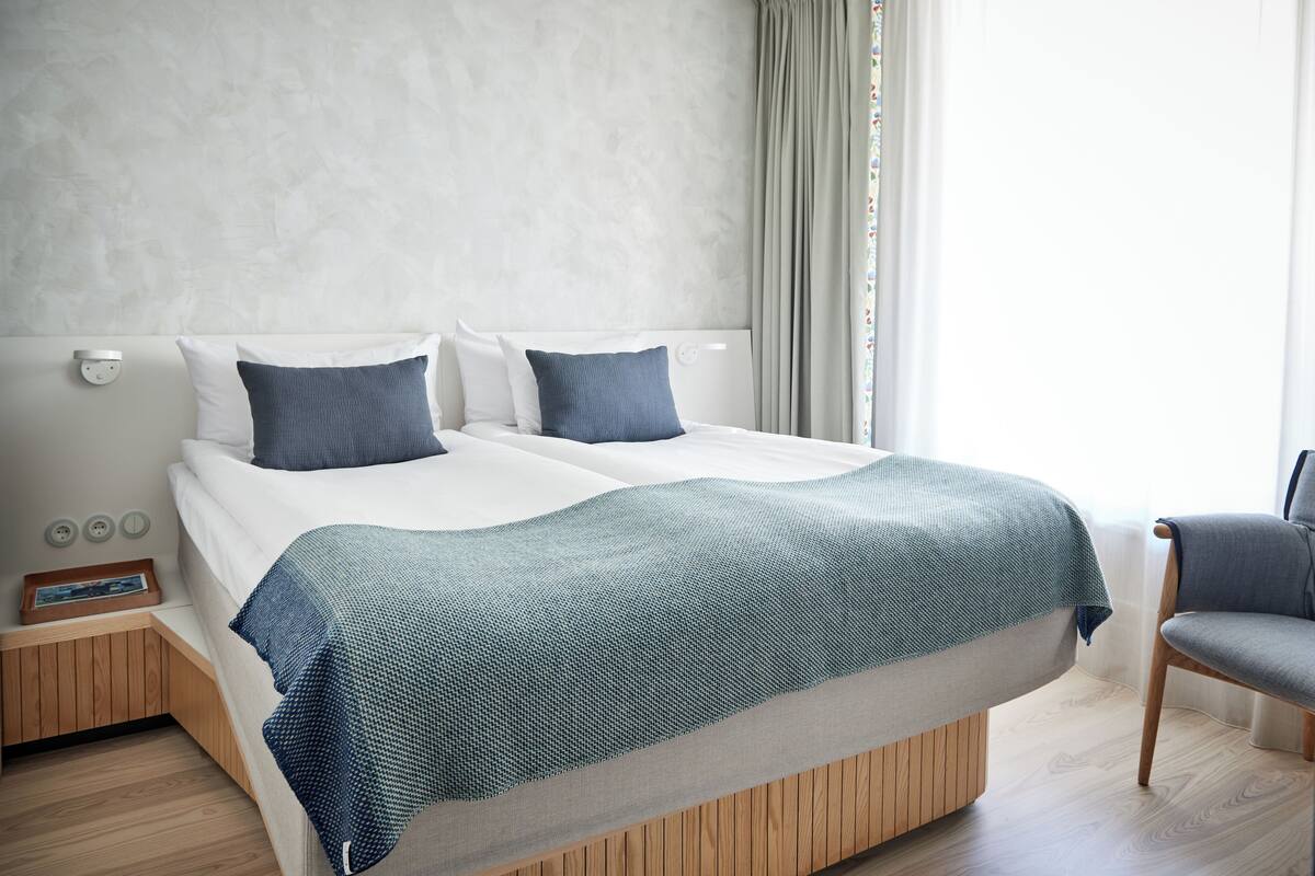 A modern hotel room with a large bed, a bedside table, and a chair.