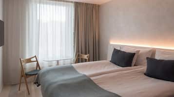 A hotel room with two beds, a small table, a chair, and a large window with curtains.