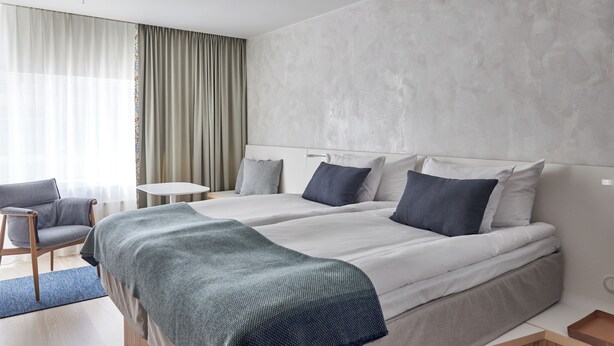 A modern hotel room with two beds, a small table, a chair, and a view of the outdoors. - Nordic Light Hotel (Stockholm)