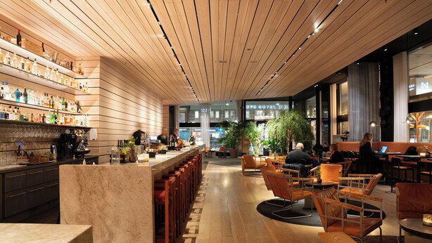 Un área de bar moderna con techo de madera, mostrador de mármol y asientos con sillas anaranjadas.