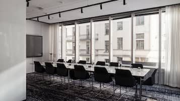 A conference room with a large table, black chairs, a projector screen, and large windows with a view of buildings.