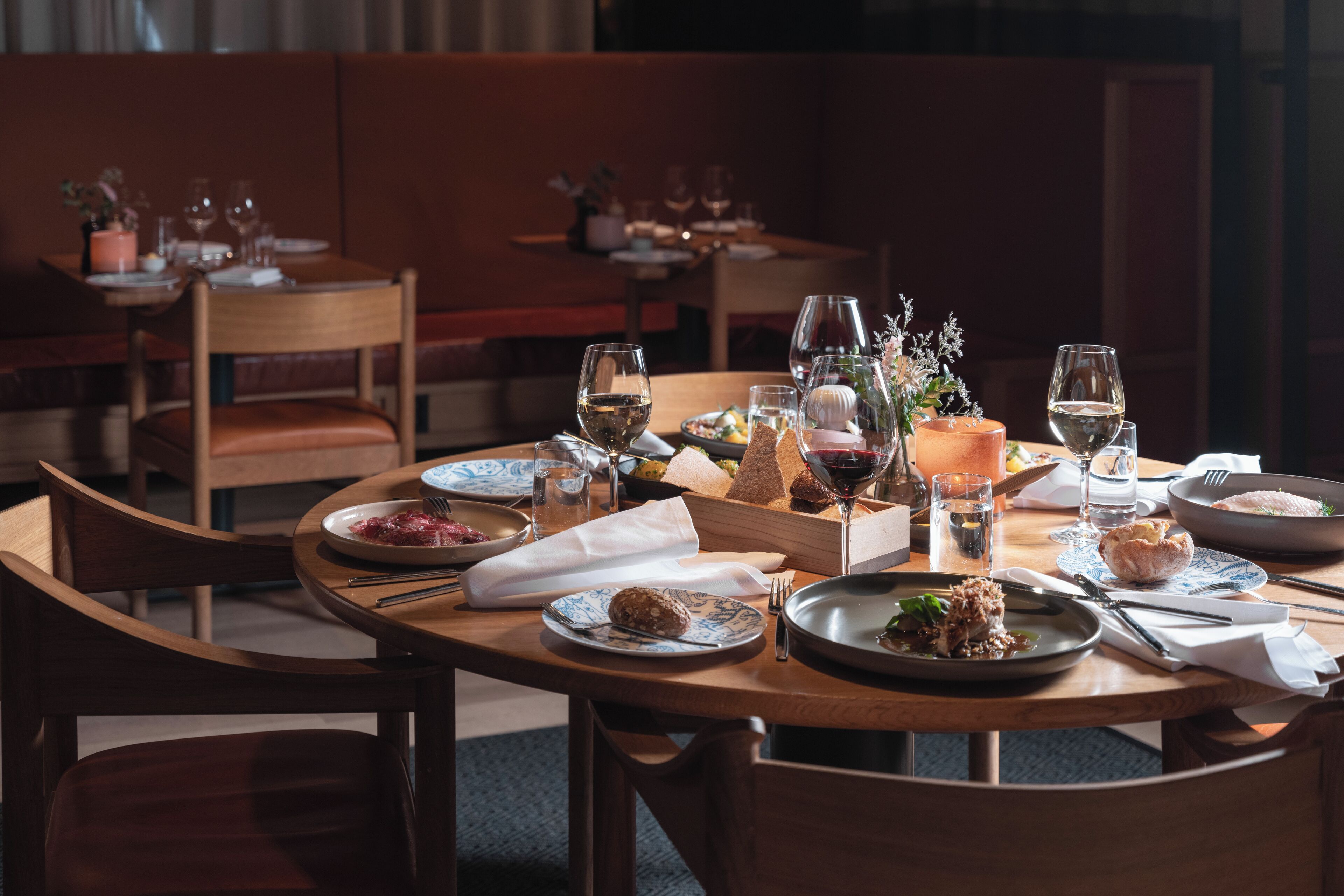 A restaurant setting with wooden tables, chairs, and a variety of dishes and drinks.
