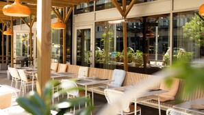 Un café al aire libre con mobiliario blanco y lámparas colgantes naranjas.