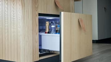A wooden cabinet with a built-in refrigerator, containing a bottle of champagne and a glass.