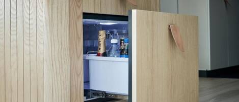 A wooden cabinet with a built-in refrigerator, containing a bottle of champagne and a glass.