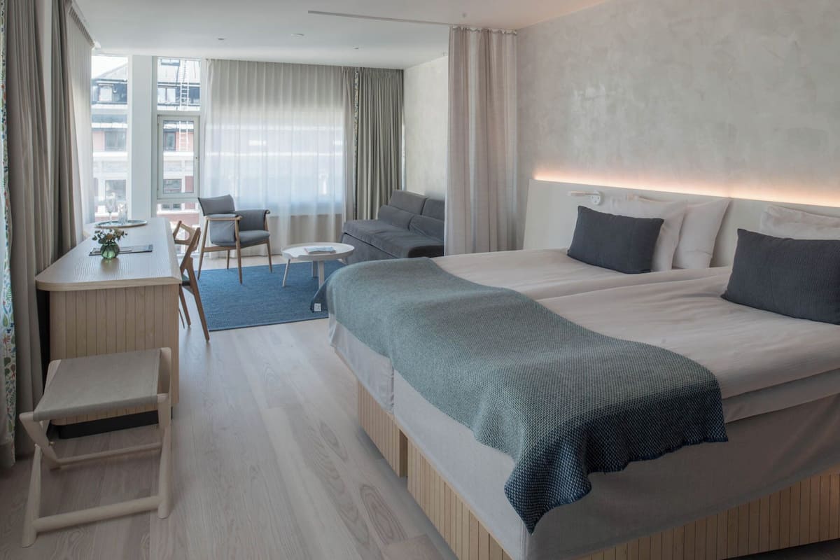 A modern hotel room with a large bed, a desk, a chair, and a sofa.