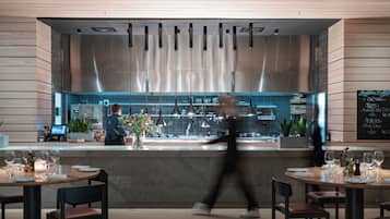 L’intérieur d’un restaurant moderne, avec un bar, des tables dressées avec des verres à vin et des assiettes, et un tableau affichant le menu au mur.