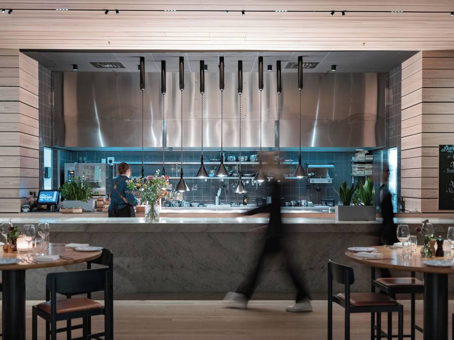 L’intérieur d’un restaurant moderne, avec un bar, des tables dressées avec des verres à vin et des assiettes, et un tableau affichant le menu au mur.