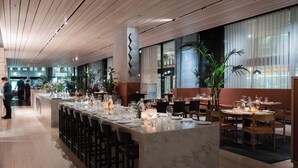 Un restaurante moderno con una barra larga, varias mesas para comer y un techo alto con paneles de madera.