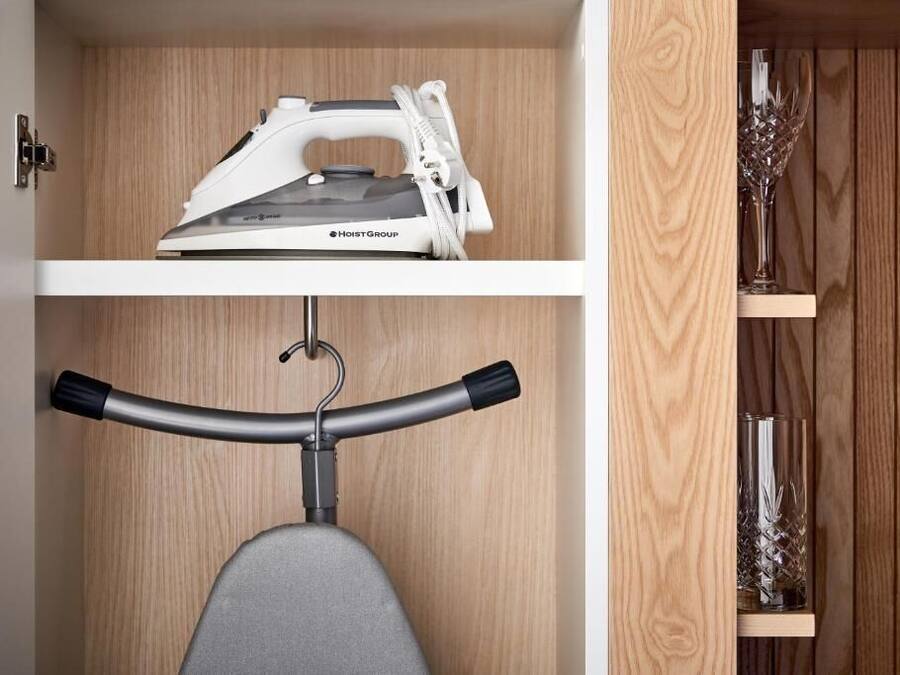 A compact storage unit with a built-in ironing board and a shelf for decorative items.