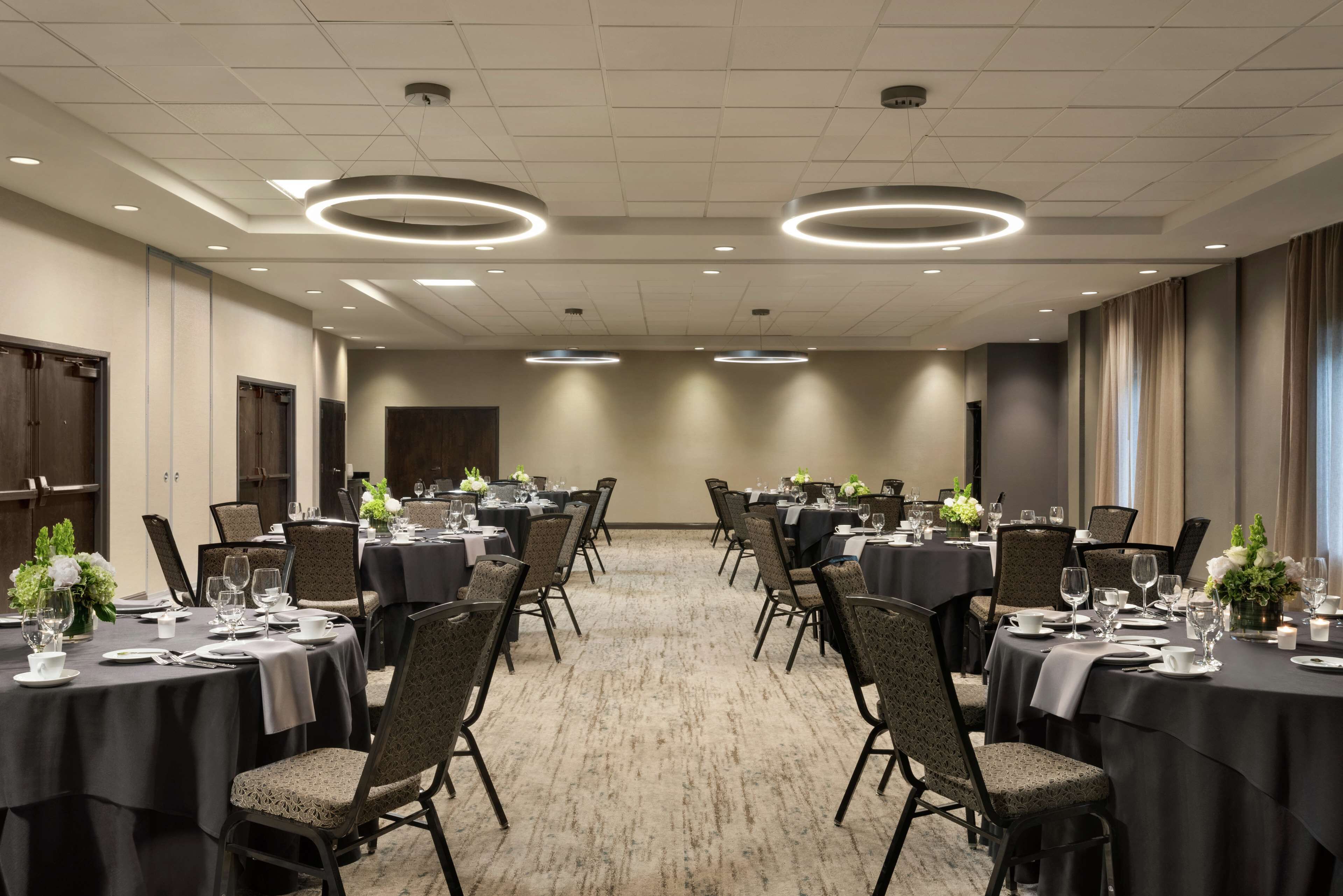 Uma sala de conferências com mesas redondas, cadeiras e centros de mesa florais.