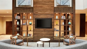 A modern living room with a TV, bookshelves, and seating. - Embassy Suites by Hilton Atlanta Alpharetta (Alpharetta)