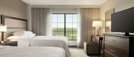 A hotel room with two beds, a TV, a desk, and a window with curtains.