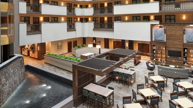 A multi-level hotel atrium with a central water feature, multiple dining areas, and balconies with plants. - Embassy Suites by Hilton Atlanta Alpharetta (Alpharetta)