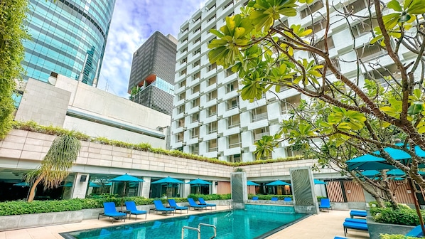 A modern hotel with a swimming pool, lounge chairs, and a view of surrounding buildings.