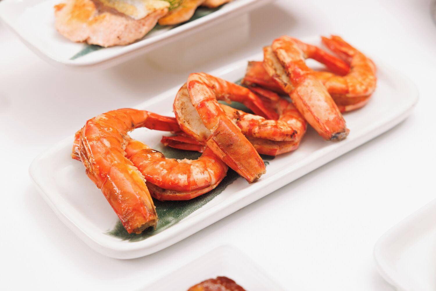 A white rectangular plate with cooked shrimp arranged on a green leaf garnish.