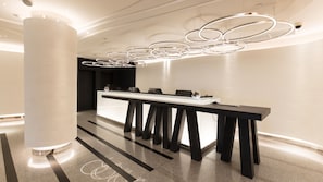 A modern reception area with a long reception desk, black chairs, and a unique circular light fixture above. - Holiday Inn Bangkok by IHG (Bangkok)