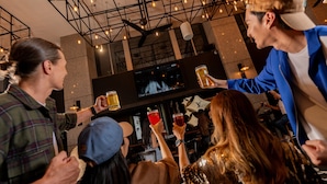 A group of people in a bar with a TV screen, holding drinks.