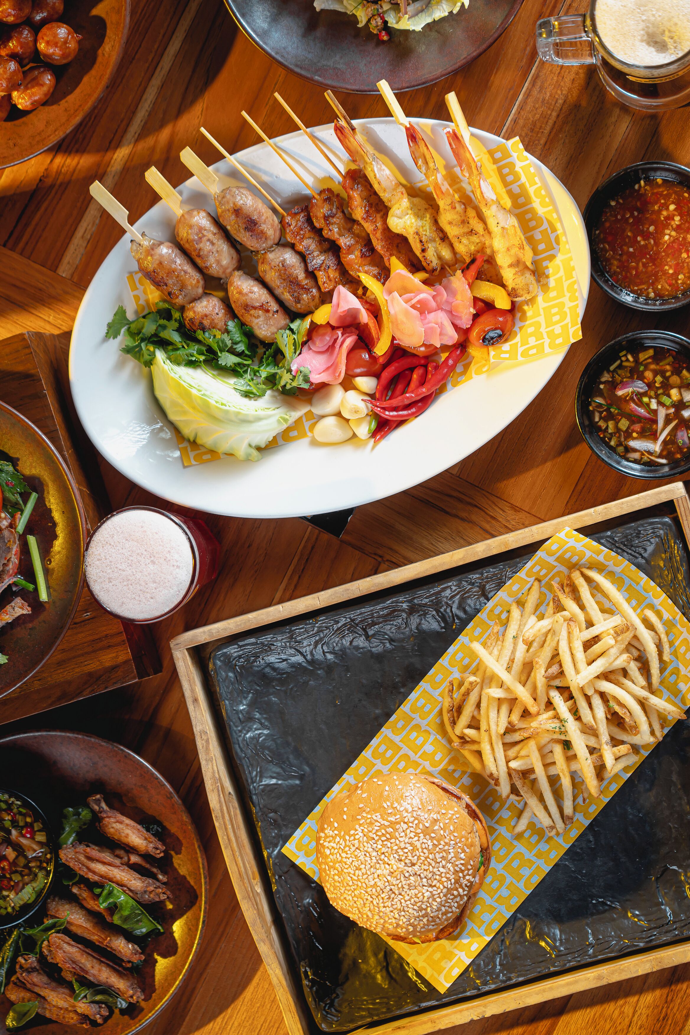 A variety of food items including skewers, a burger, fries, and a salad on a wooden table.