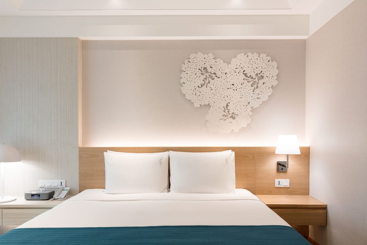 Una camera d'hotel con un letto, comodini, una decorazione a forma di cuore appesa al muro e un tavolino notte con una lampada.