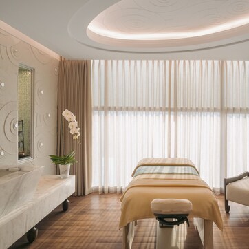 A modern hotel room with a bed, a sitting area, a vanity with a mirror, and a small table with a plant.