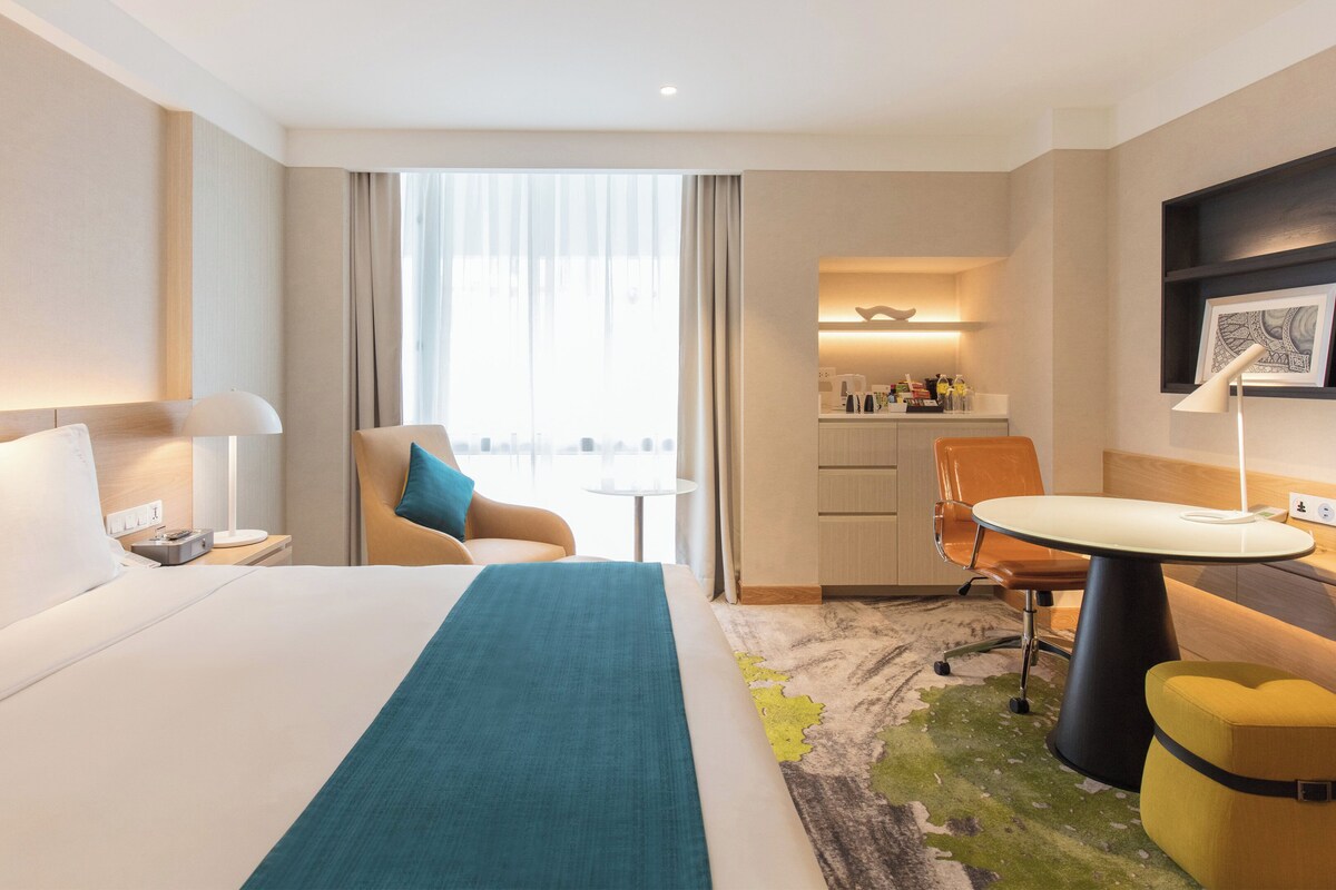 Hotellihuone, jossa on sänky, työpöytä, tuoli, pieni pöytä ja pieni keittiö.