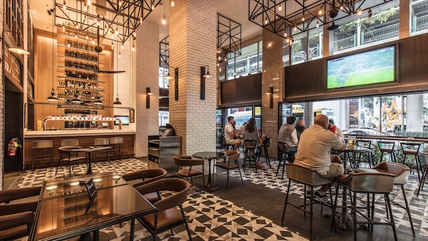 A modern bar area with a checkered floor, bar stools, and a large screen displaying a sports game. - Holiday Inn Bangkok by IHG (Bangkok)