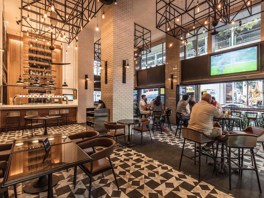 Un área de bar moderna con suelo a cuadros, taburetes y una pantalla grande mostrando un evento deportivo.