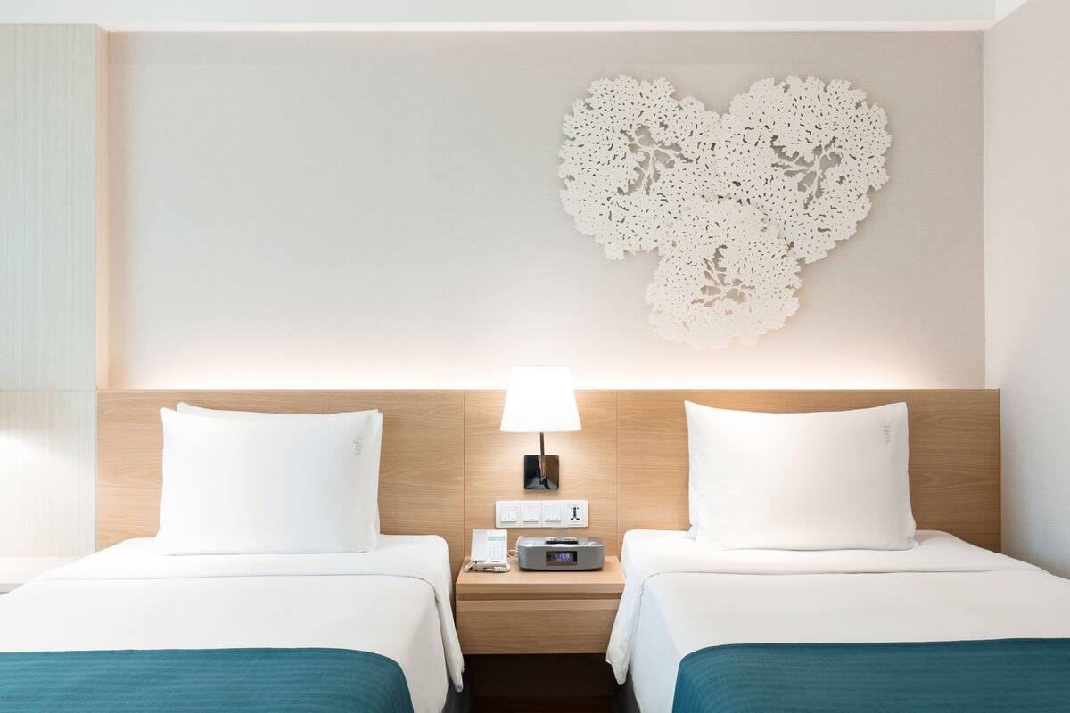 Una camera d'albergo con due letti, un comodino con una lampada e un elemento decorativo a parete.