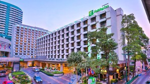 A Holiday Inn hotel with a modern design, featuring a central courtyard with palm trees and a roundabout for traffic. - Holiday Inn Bangkok by IHG (Bangkok)