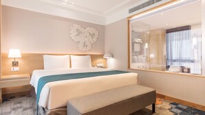 A hotel room with a large bed, bedside tables with lamps, a bench, a decorative wall piece, and a large mirror.