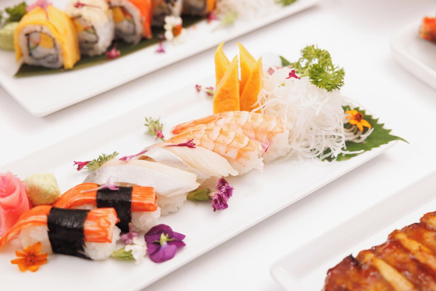 A variety of sushi dishes on white rectangular plates, each garnished with different ingredients and flowers.
