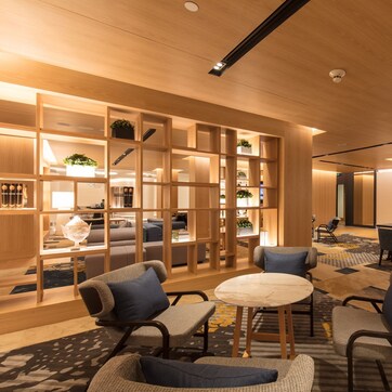 A modern hotel lobby with wooden shelving, comfortable seating, and a central dining area.