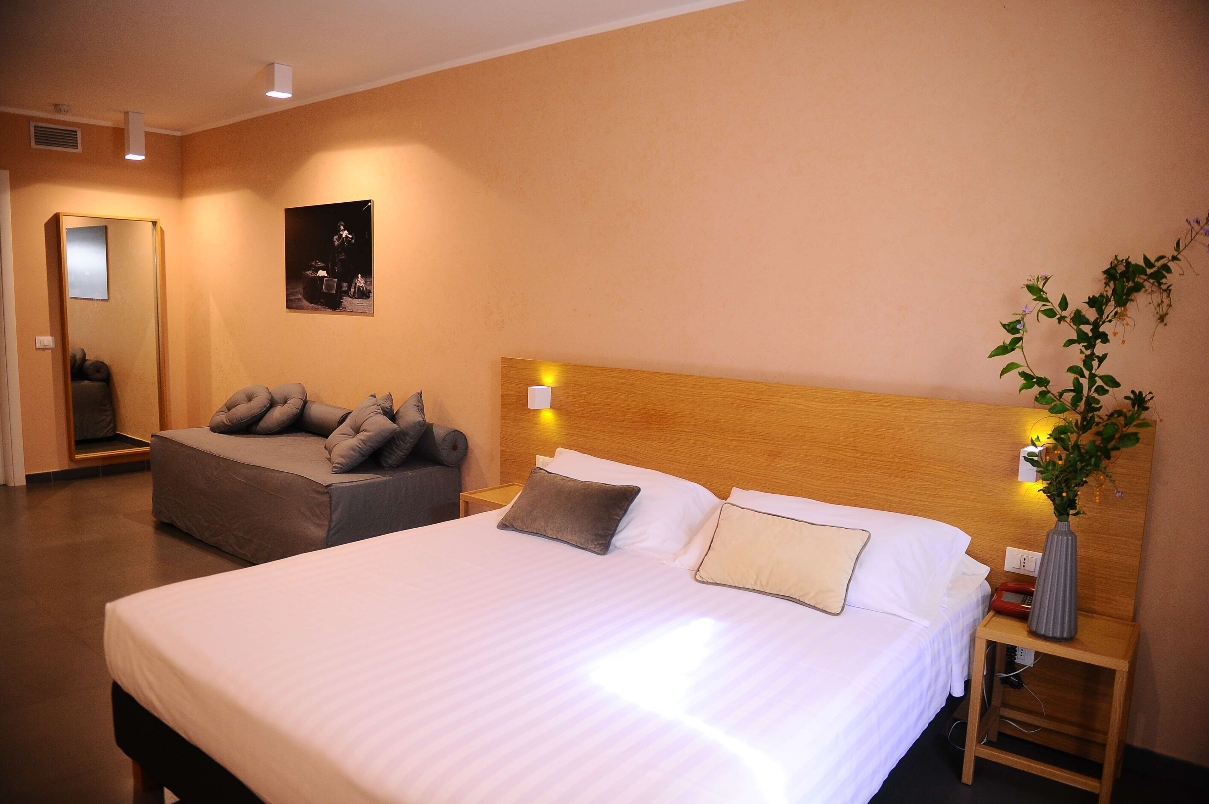 A hotel room with two beds, a nightstand with a vase of flowers, and a poster on the wall.