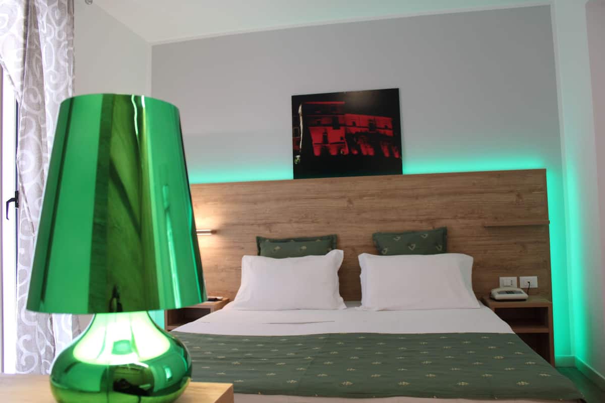 A hotel room with a wooden headboard, two pillows, a green lamp, and a bed with a green bedspread.
