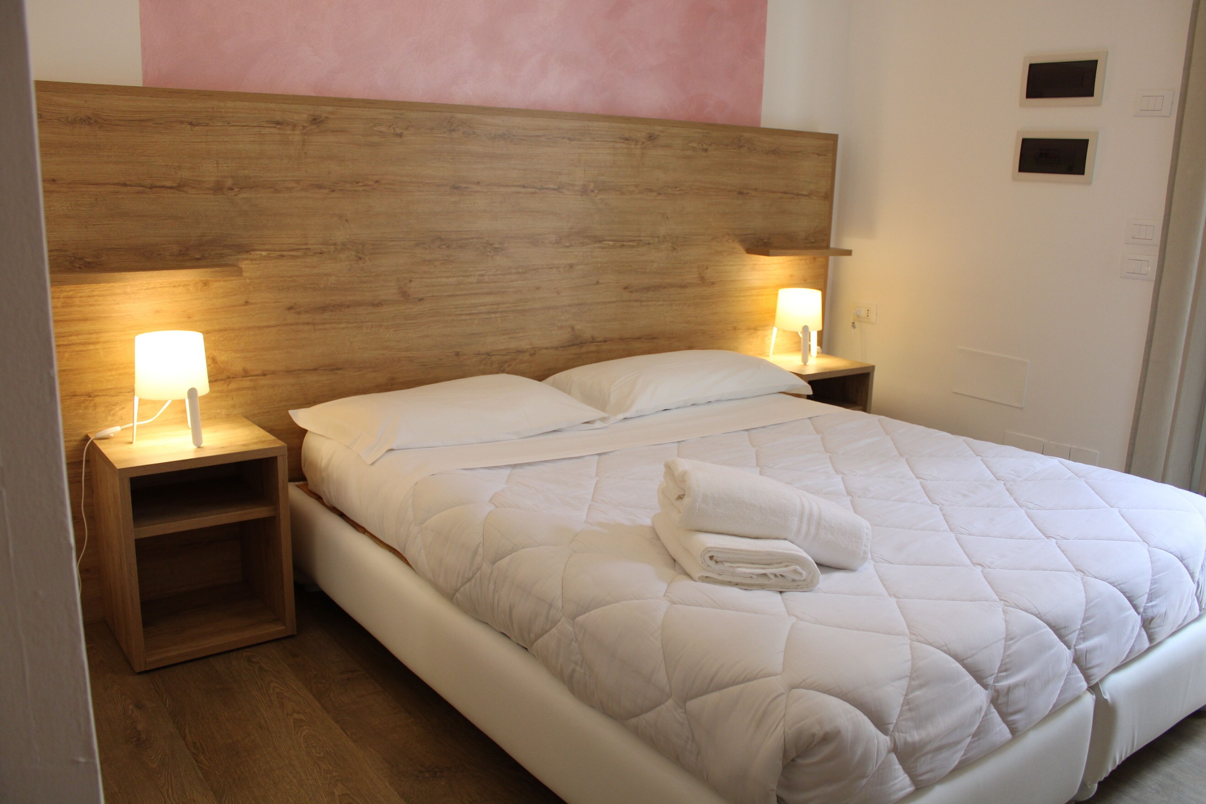A neatly made bed with a wooden headboard, two bedside tables with lamps, and a folded towel on the bed.