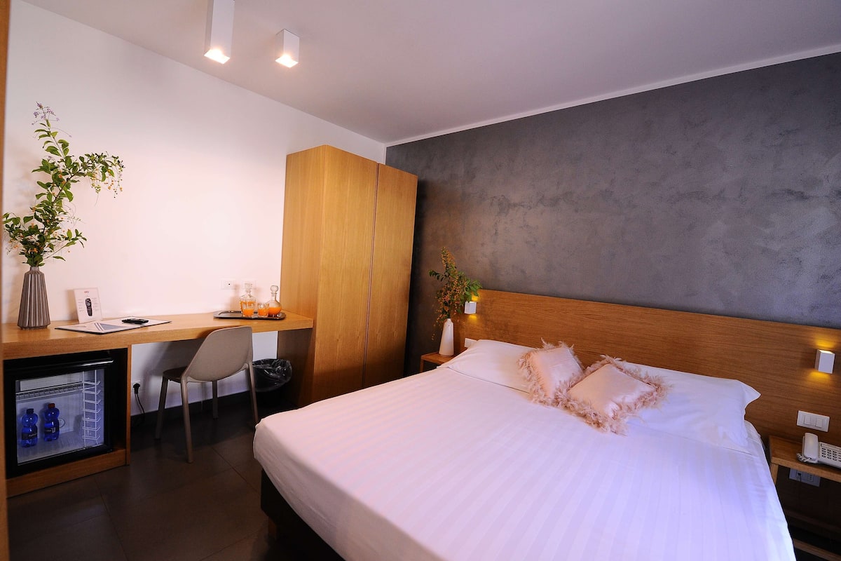 A hotel room with a bed, a desk, a chair, a wardrobe, and a small refrigerator.