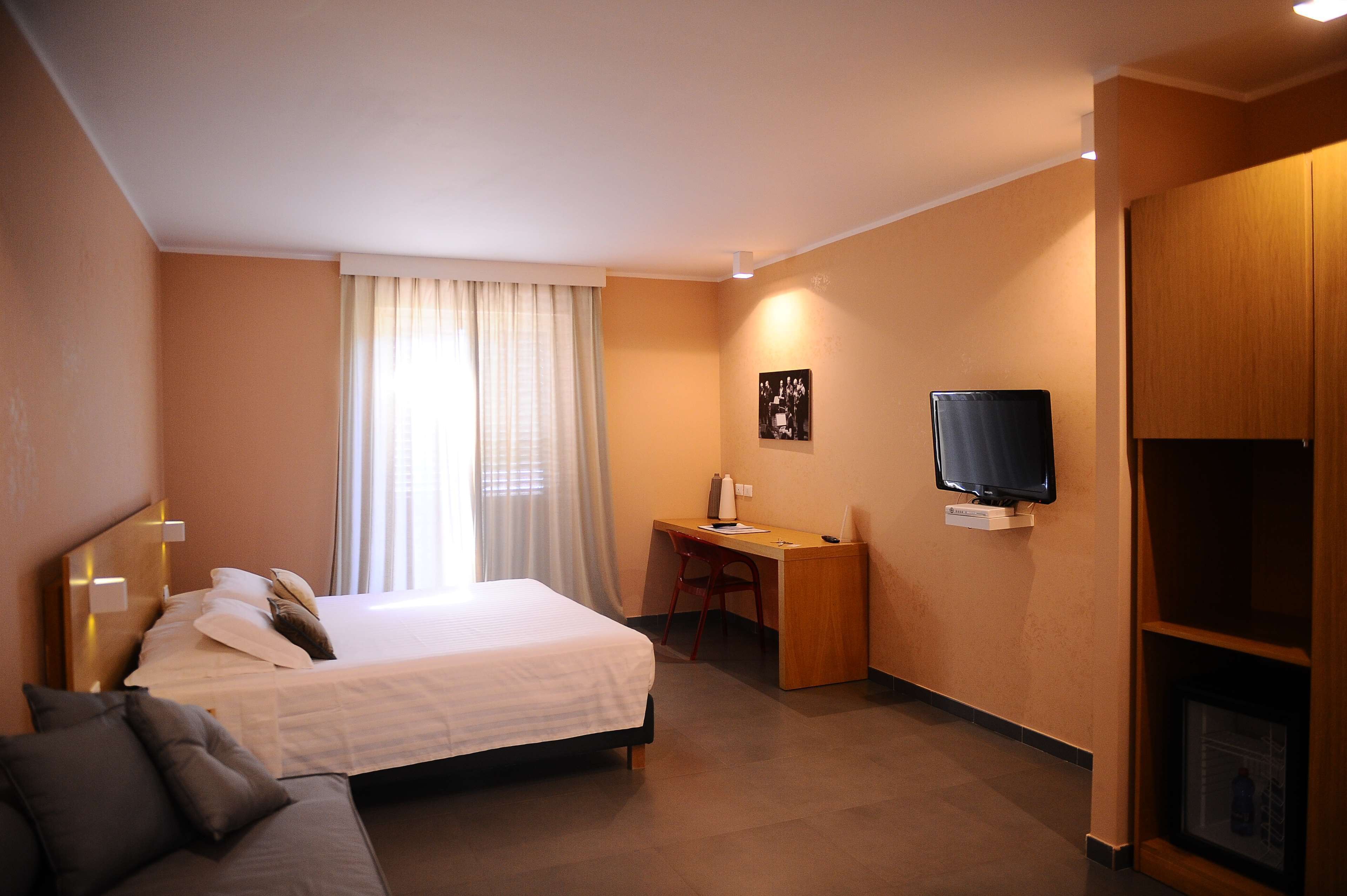 A hotel room with a bed, a desk, a television, and a wardrobe.